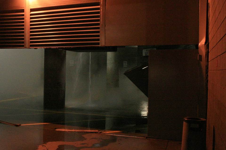 Hot water and steam pouring from an opening in a basement ceiling onto a flooded floor, lit by a single lamp
