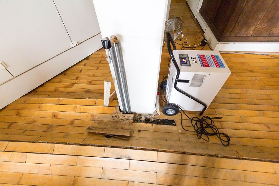 Swollen wood parquet floor around a white column, a portable dehumidifier and its power cord standing beside it