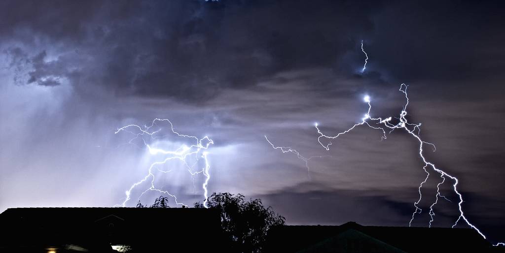 Forked lightning under dark storm clouds over the Las Vegas valley at night, rooftops in silhouette below
