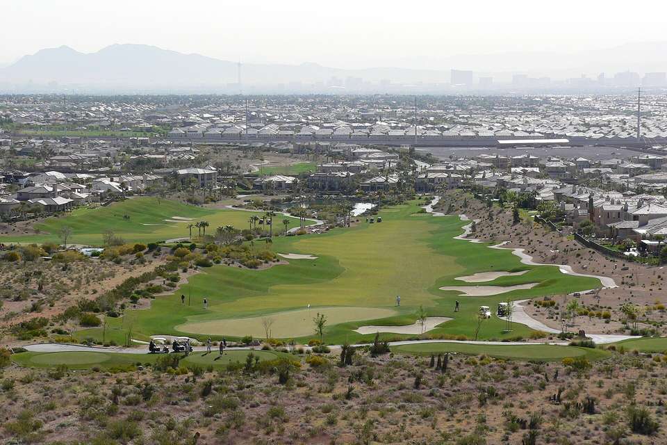Green golf fairways and sand bunkers among desert scrub, with rooftops and the Las Vegas valley in the hazy distance